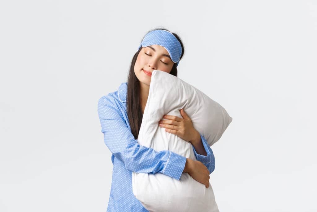 charming sleeping asian girl eyemask pyjama hugging pillow lying it with closed eyes dreaming having night sleep posing white background dreamy copy space